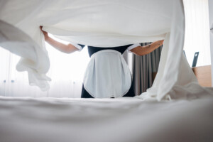 Professional hotel housekeeping depicted as a staff member tidies bed linens in a bright room.