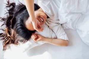 Relaxed morning: A young woman laughing cheerfully in a freshly made white bed, her dark hair spread out on the pillow.