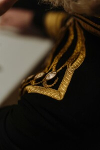 A person wearing black clothing with gold, ornately decorated shoulder pieces.