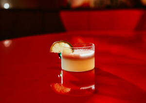 A glass with a creamy drink and an orange slice stands on a glossy red table.